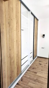 Otevřené posuvné dveře v dekoru dubu a bílý vnitřek skříně s policemi a zásuvkami